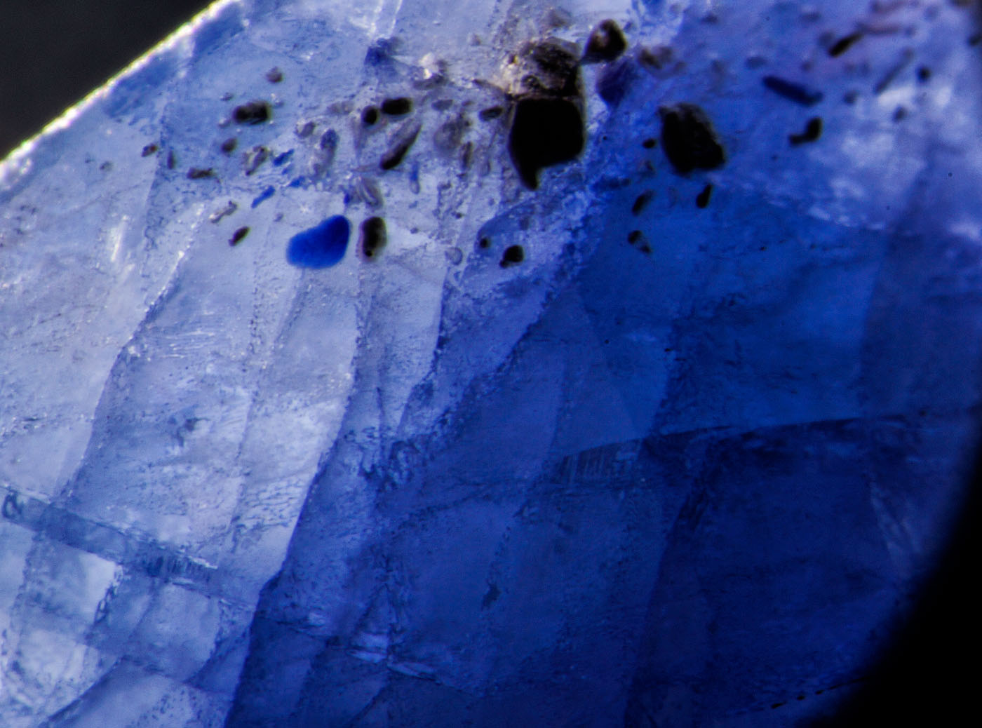 Figure 5. Left: Blue pool of cobalt-doped glass fills a surface cavity in this first-generation Tanusorn stone. Dark-field illumination. Right: The same inclusion in reflected light reveals the lower luster of the glass filler. Oblique fiber-optic illumination. (Photos: Richard Hughes). Lotus Gemology.