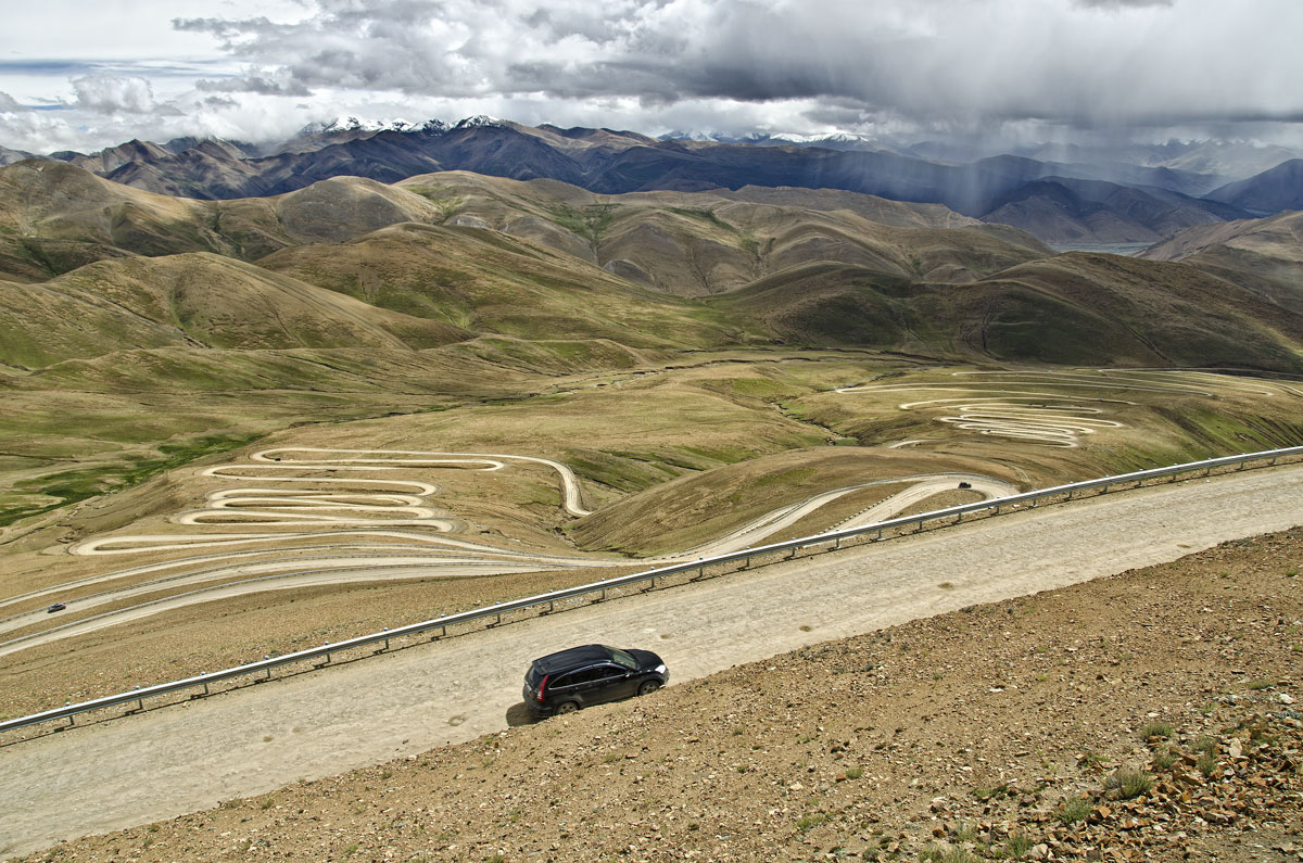 Twistin' an' turnin' in Tibet At 8848 m (29,028 ft), Mount Everest lies in a region that contains many of the world's highest peaks. The northern base camp is eight hours' drive west of Shigatse, with the road winding over two major passes. In this photo, taken atop Pang La (5050 m; 16,568 ft), Everest lies behind the clouds in the distance.&nbsp;Photo: Richard W. Hughes