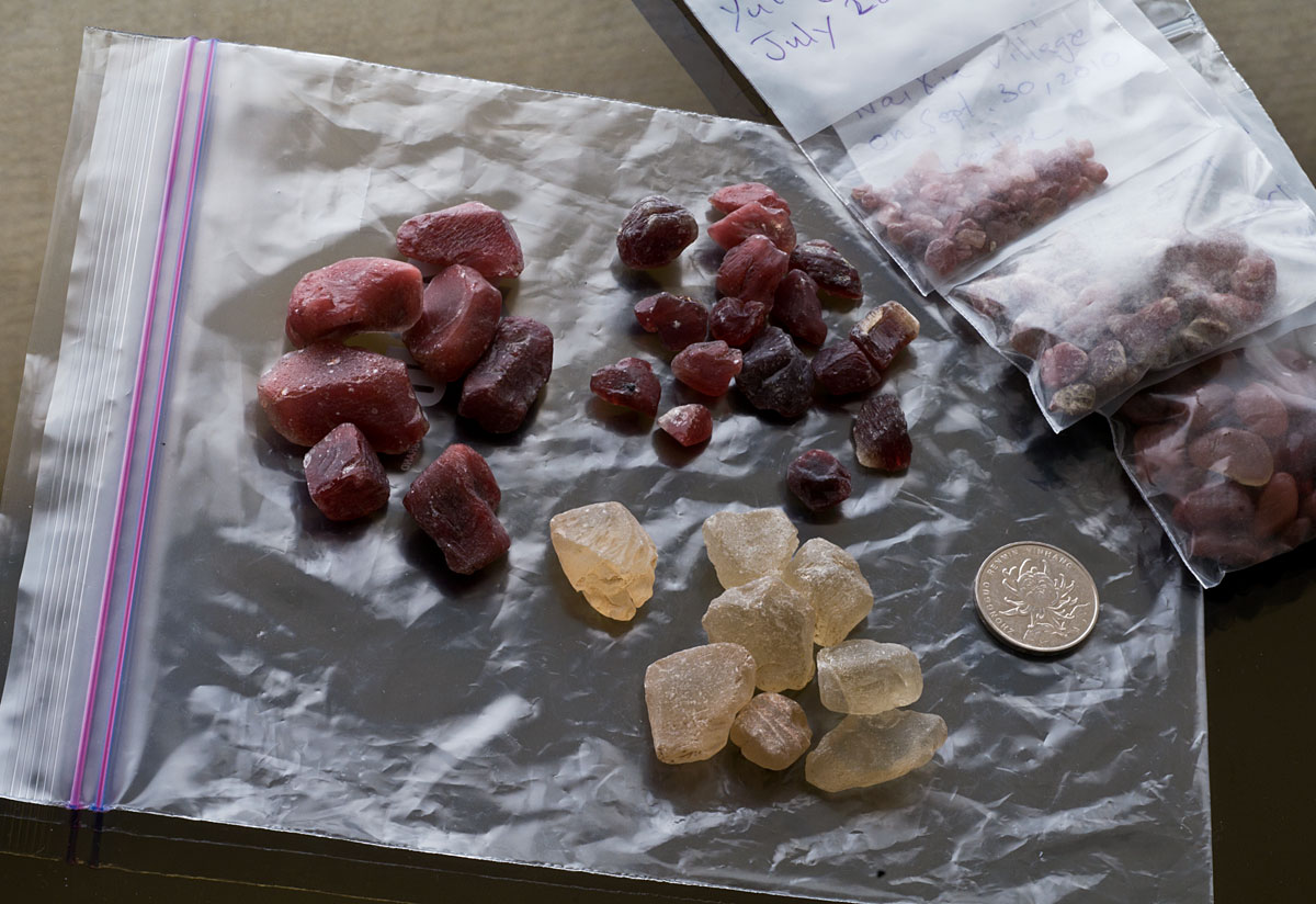 Figure 3. Pale yellow untreated andesine said to come from Inner Mongolia, flanked by two lots of deep red treated andesine. The three bags of rough on the right are natural Tibetan andesine. Untreated and treated Inner Mongolian andesines courtesy of Marco Cheung of Litto Gems. Photo: Wimon Manorotkul