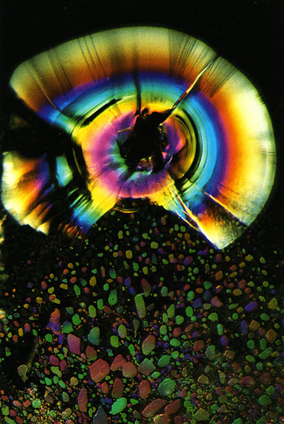 The iridescent aura of a stress fracture extends outward from a solid inclusion, while an audience of liquid droplets bows in reverence below. Beryl, page 326.