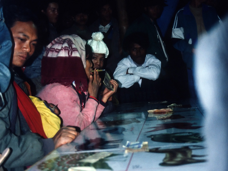 The small village of Makapin lies on the southern edge of Burma's jade-producing area. Because it is a mining town with a strong Chinese influence, the main nightly entertainment is gambling. Mah-jongg might be expected since Makapin is so close to the Chinese border; the betting game certainly is popular. Unexpected was a huge roulette wheel marked with Chinese animal symbols and crowded with a group of anxious bettors. All these activities are lighted by candles or by small generator-powered fluorescent bulbs