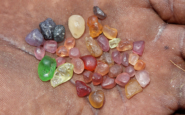 A Tunduru miner presents gems from his mine on the Muhuwesi river: a piece of tsavorite is shown next to garnets, spinels, chrysoberyl and sapphire. Photo: V. Pardieu/Gübelin Gem Lab, 2007.